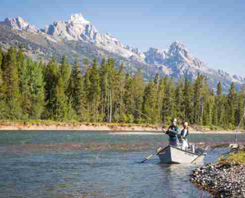 people in a boat fishing on the river with trees in the background