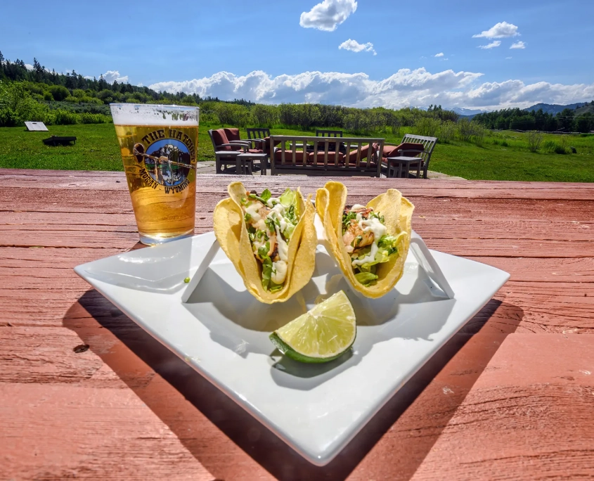 tacos and a lime on a plate with a beer outside at a table